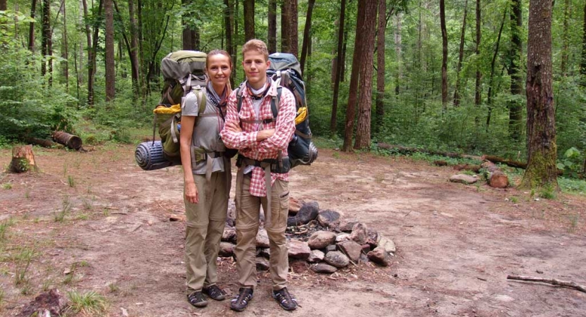 a parent and their child are wearing backpacking gear while smiling at the camera on an outward bound course in north carolina